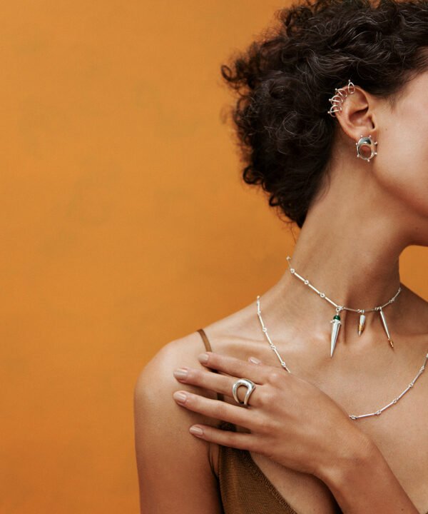 modelo con varias cadenas y dijes en plata, topos y anillos, en un ambiente amarillo. Imagen de Campaña de Colección No.4  de Aysha Bilgrami Joyeria por Daniella Benedetti