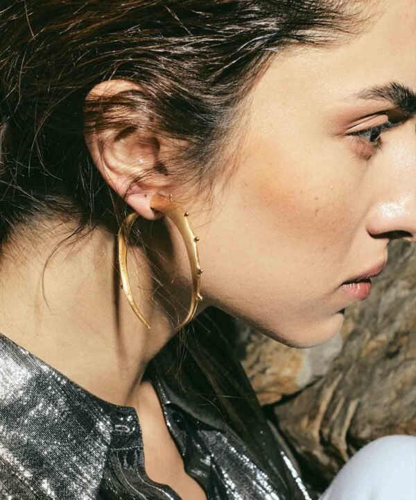 side profile of actress juana del rio wearing a silver shirt and some large crescent shape hoops imitating an expansion earring. Made in recycled silver by pakistani-colombian jewelry designer aysha bilgrami in Bogotá, colombia
