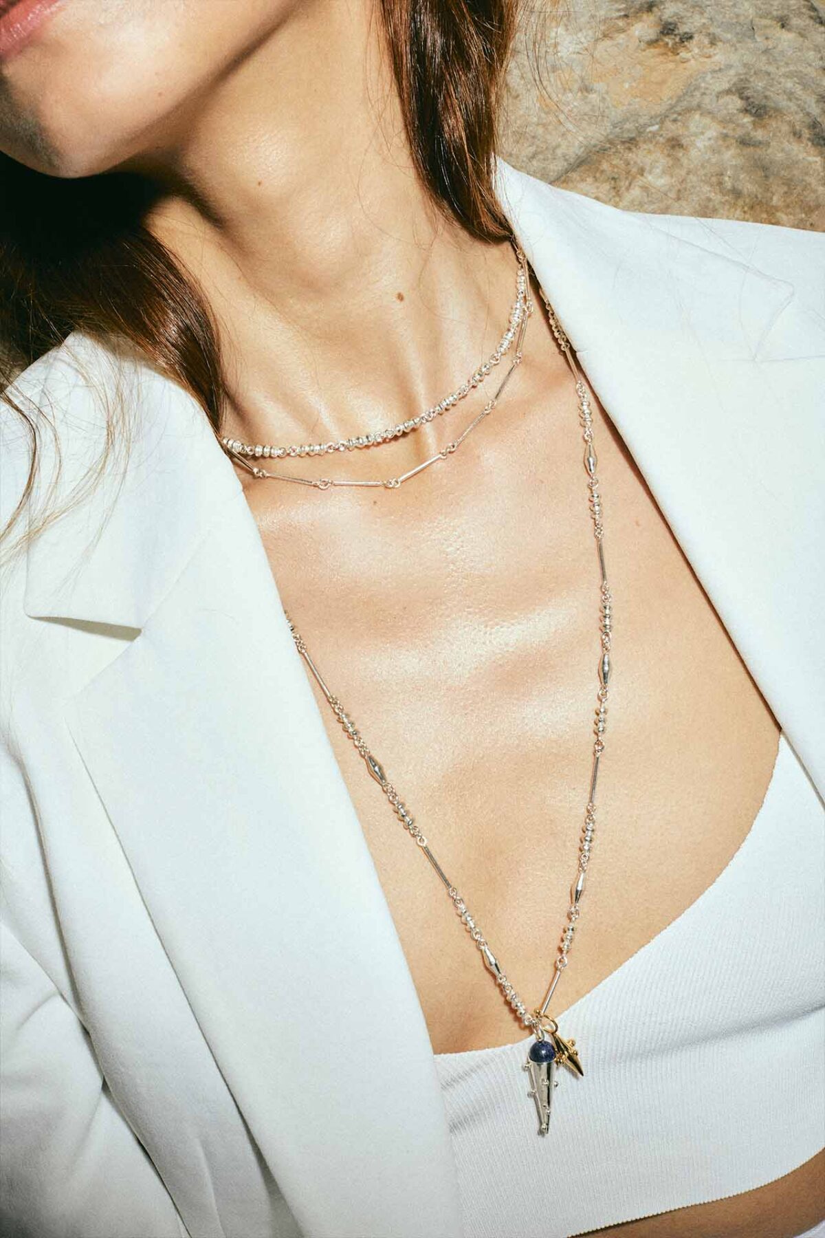 juana del rio modeling a white blazer and crop top and 3 silver chains with two hanging cone shapes pendants in silver and gold, colombian brand invited to aysha bilgrami jewelry pop up shop in bogota colombia
