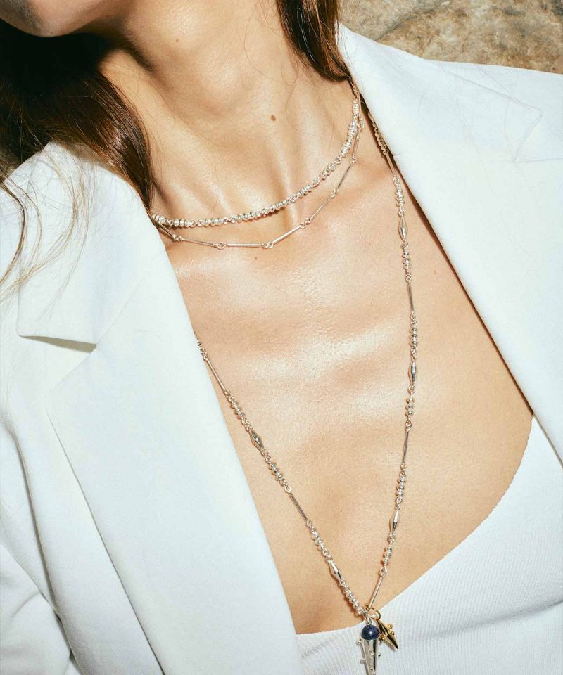 juana del rio modeling a white blazer and crop top and 3 silver chains with two hanging cone shapes pendants in silver and gold, colombian brand invited to aysha bilgrami jewelry pop up shop in bogota colombia