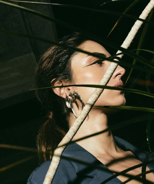 juana del rio actress behind plants modeling a stack of three crescent shape hoops. Quite and ear party. 