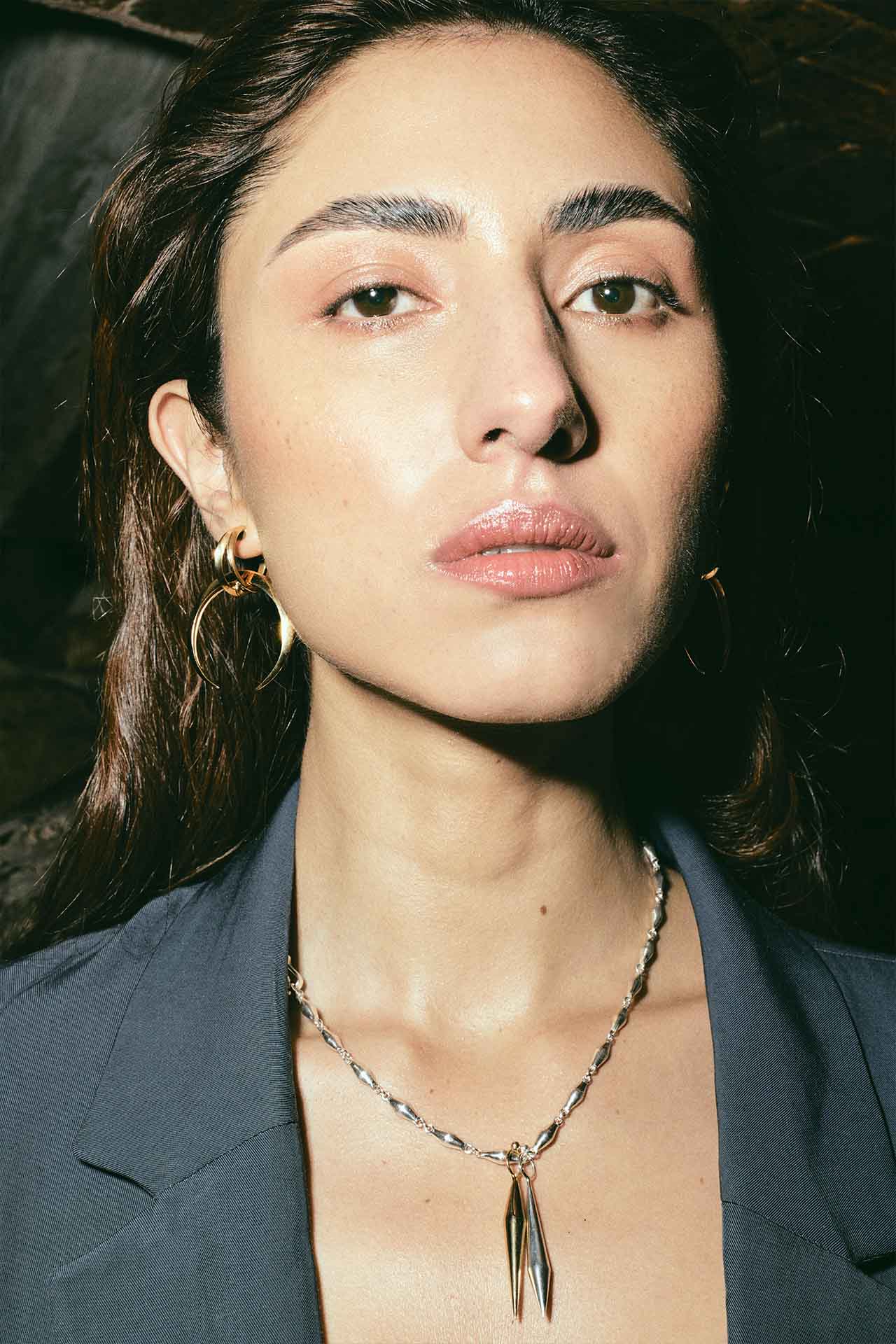 perfil de juana del río con pendientes en forma de media luna, cadena de plata con eslabones conicos y dos dijes en punta