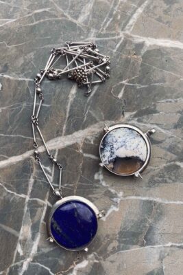 two full moon pendants with lapis lazuli and turkish opal stones over a dark stone surface, by aysha bilgrami in recycled silver